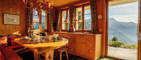 A cozy room with a wooden dining table, a red sofa, and a view of mountains through large windows.