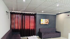 A modern living room with a sofa, a coffee table, and a TV mounted on the wall. - Hotel Elite Inn (Jodhpur)