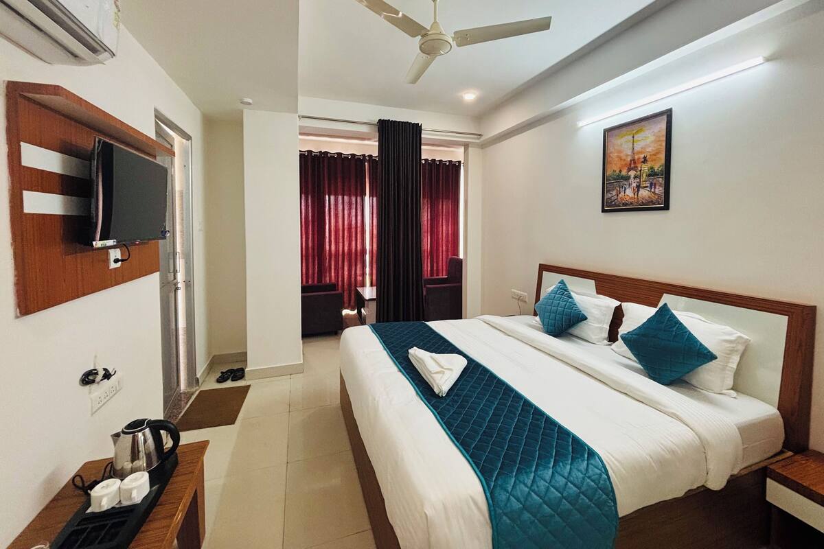 Una habitación de hotel con una cama, un televisor montado en la pared, un ventilador de techo y un cuadro colgado.