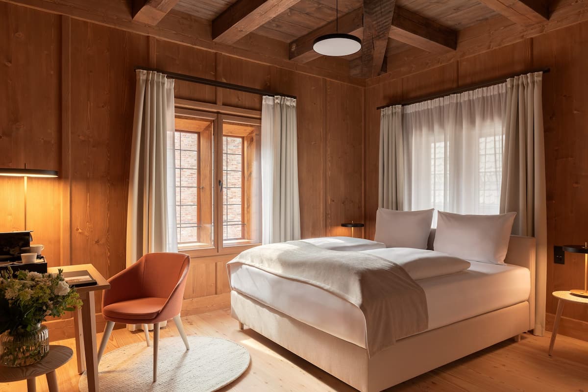 A wooden room with a bed, a chair, a table, and a lamp.