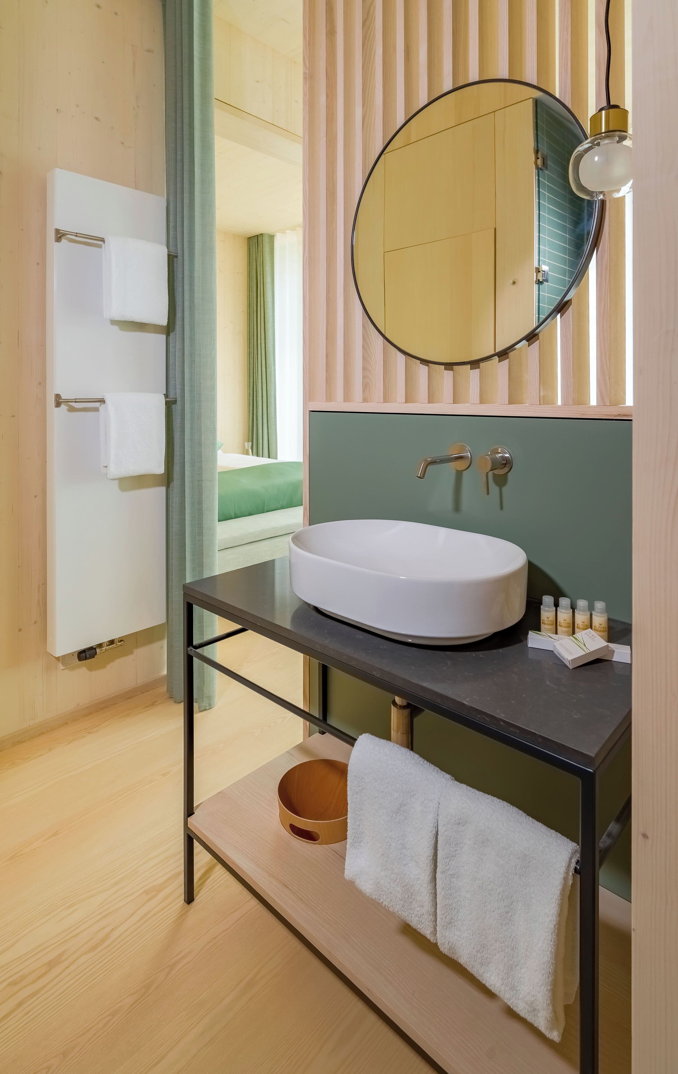 A modern bathroom with a round mirror, a white sink, and a wooden vanity.