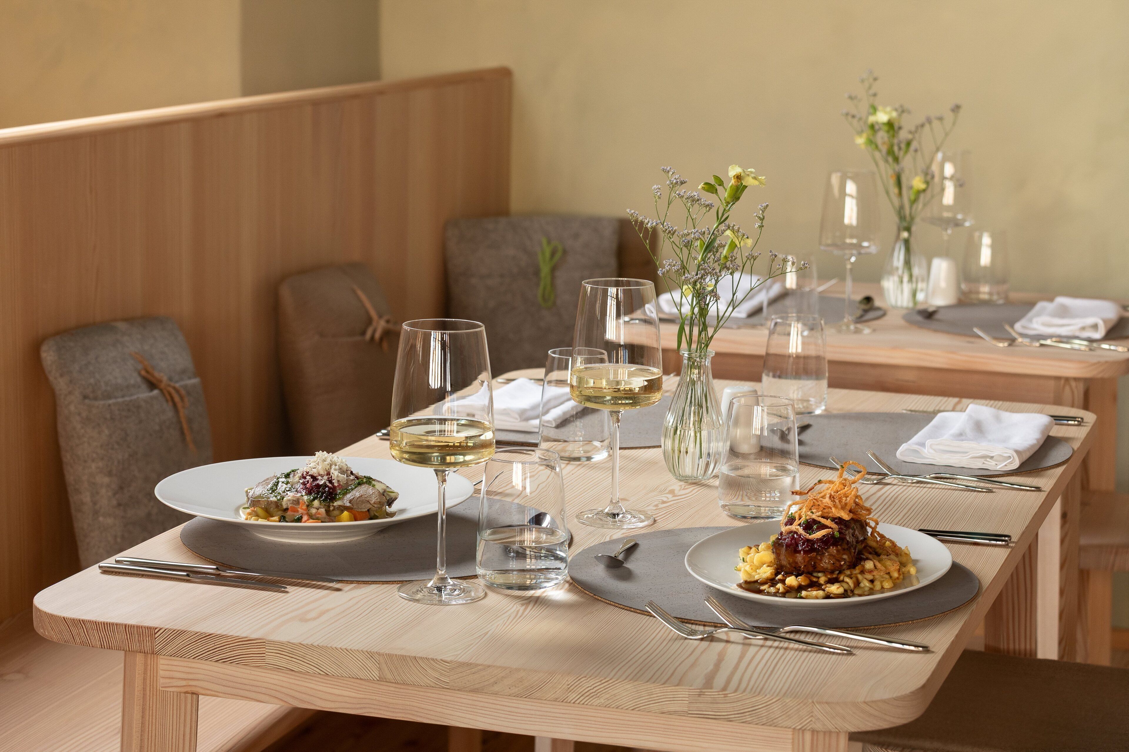 A dining table set with plates of food, wine glasses, and cutlery.
