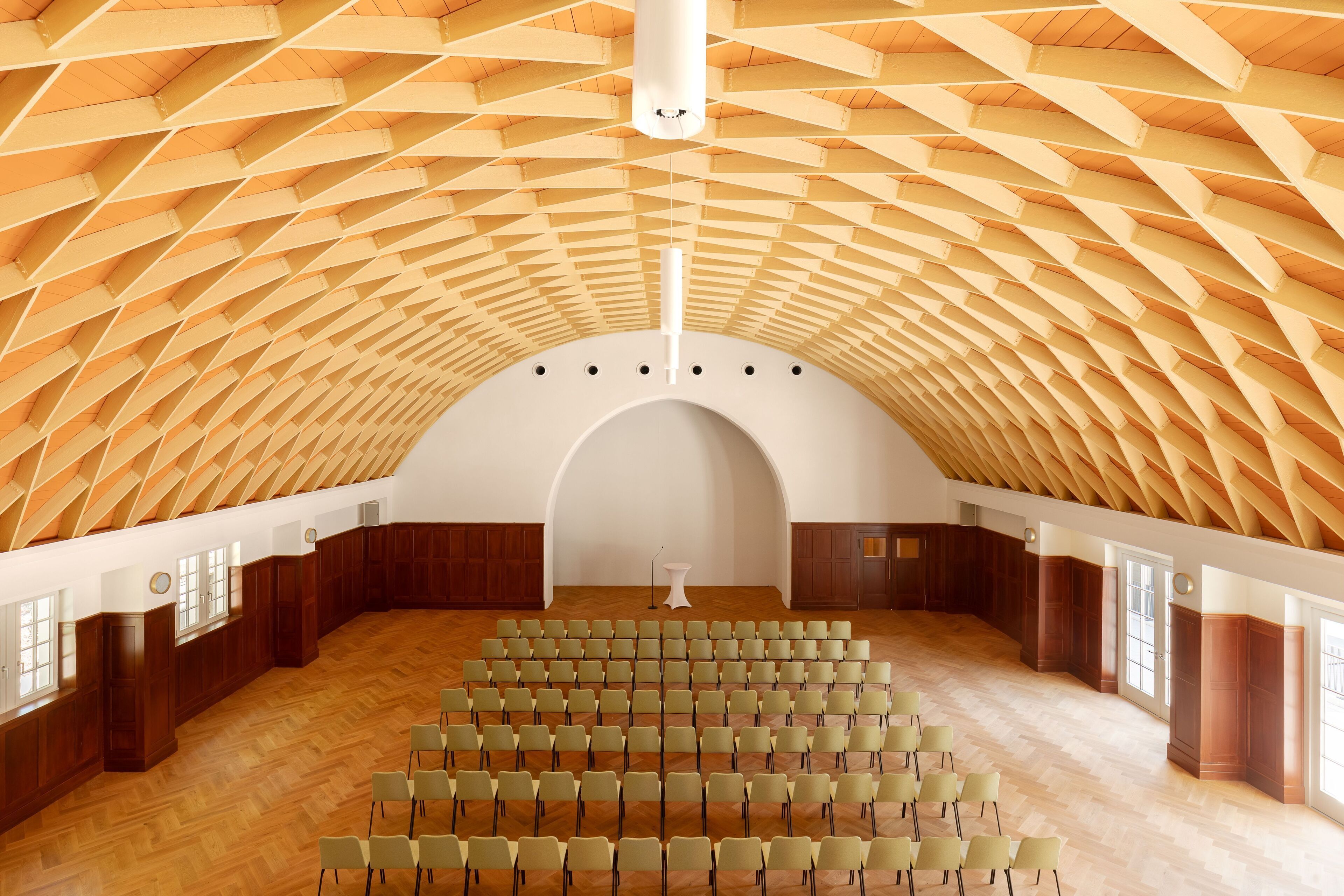 Auditorio, jossa on ainutlaatuinen, geometrisesti muotoiltu kattorakenne, useita rivissä olevia tuolirivejä ja keskeinen esiintymislava.