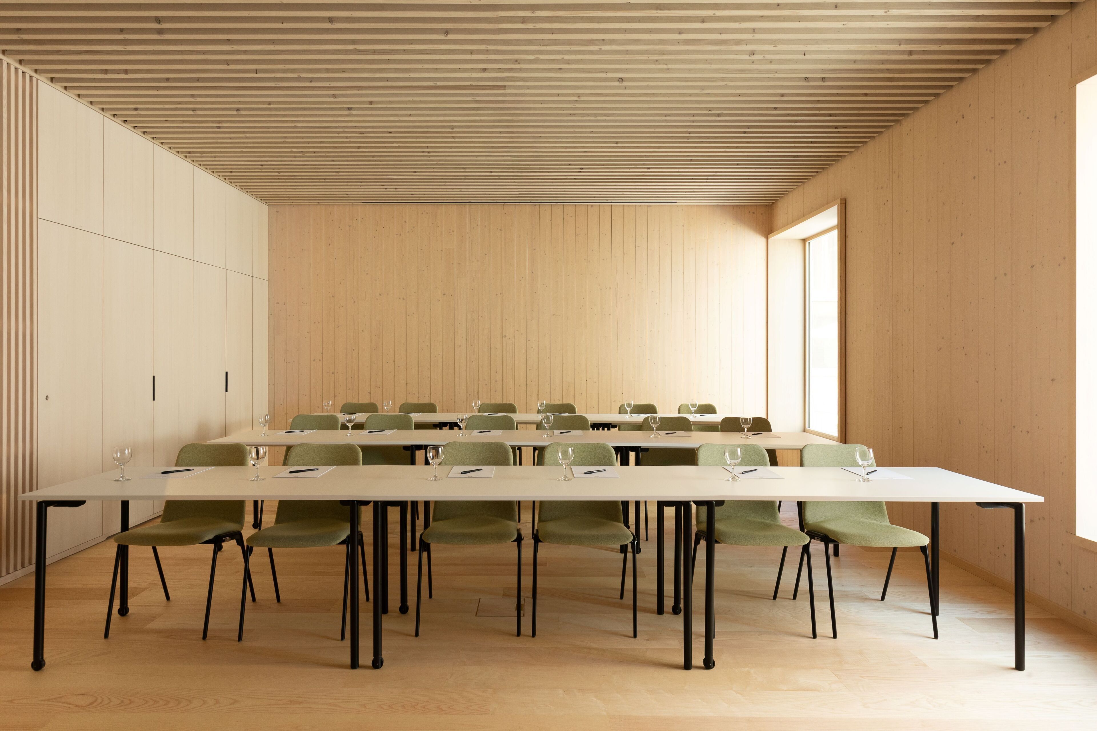 A conference room with a long table, green chairs, and a wooden ceiling.