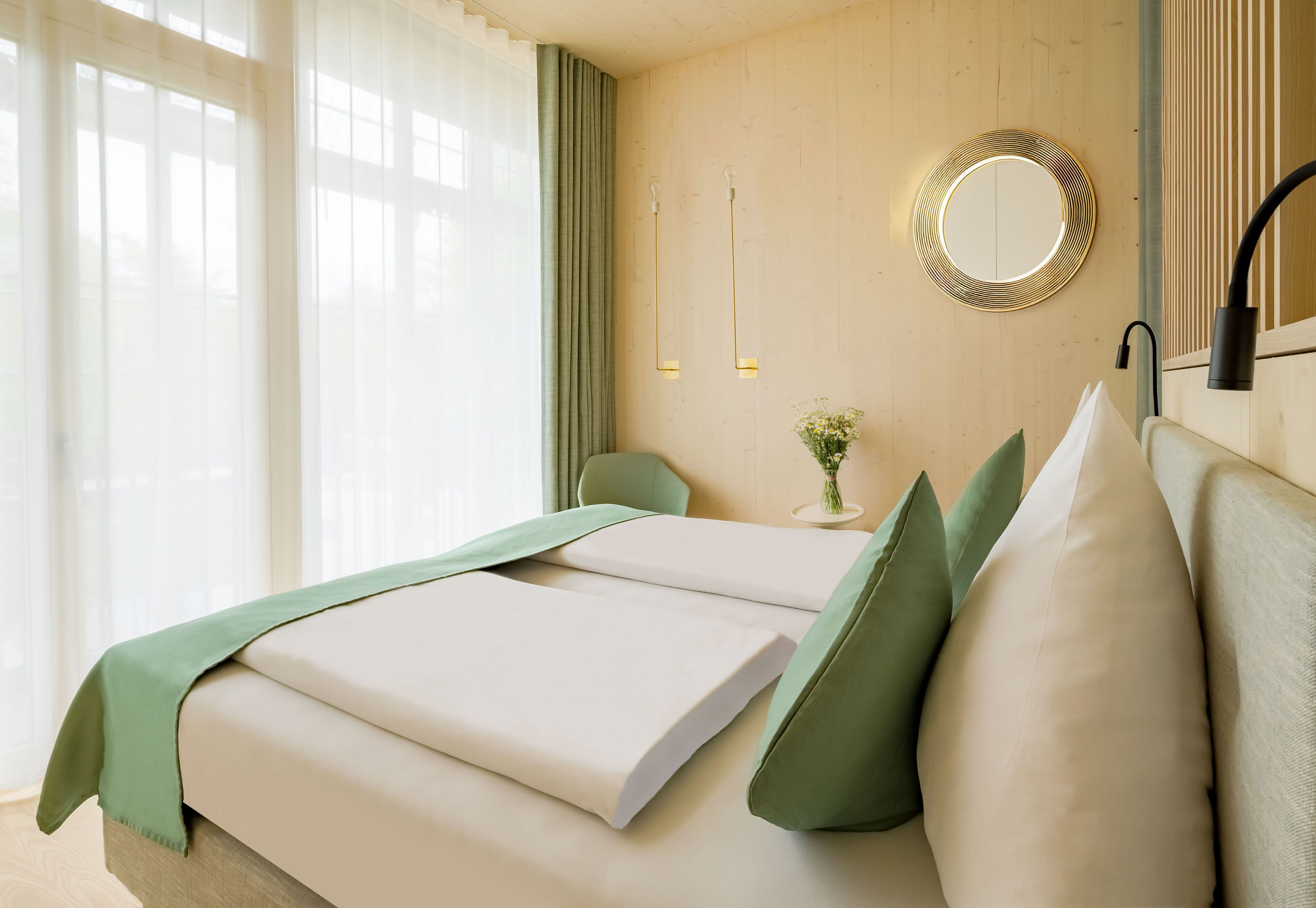 Een hotelkamer met een bed, een nachtkastje met een bloevas en een spiegel aan de muur.