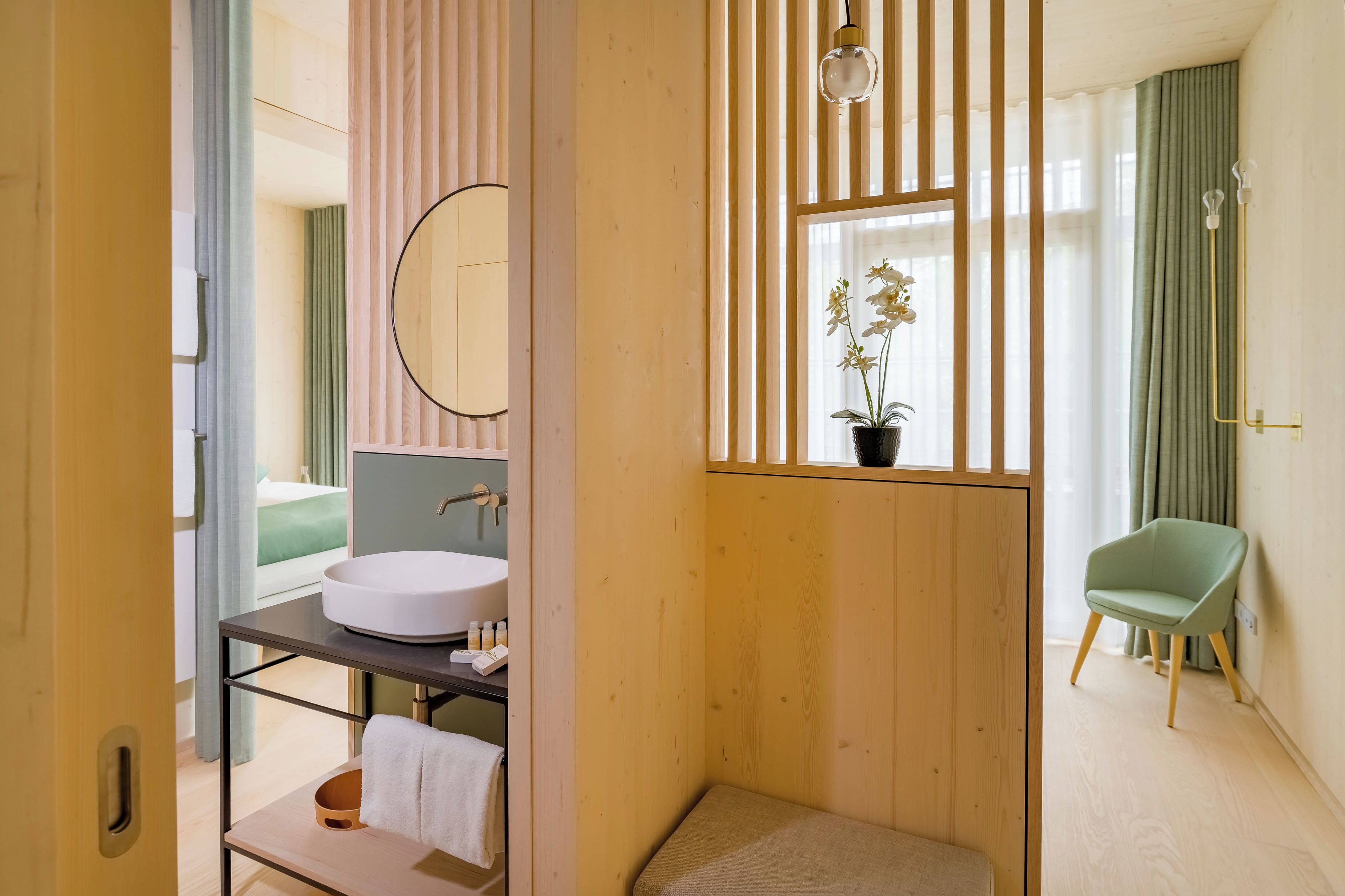 Un baño moderno con un mueble de tocador de madera, un espejo redondo y una orquídea en maceta.