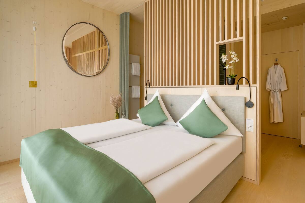 A modern hotel room with a bed, a mirror, a robe, and a wooden panel wall.