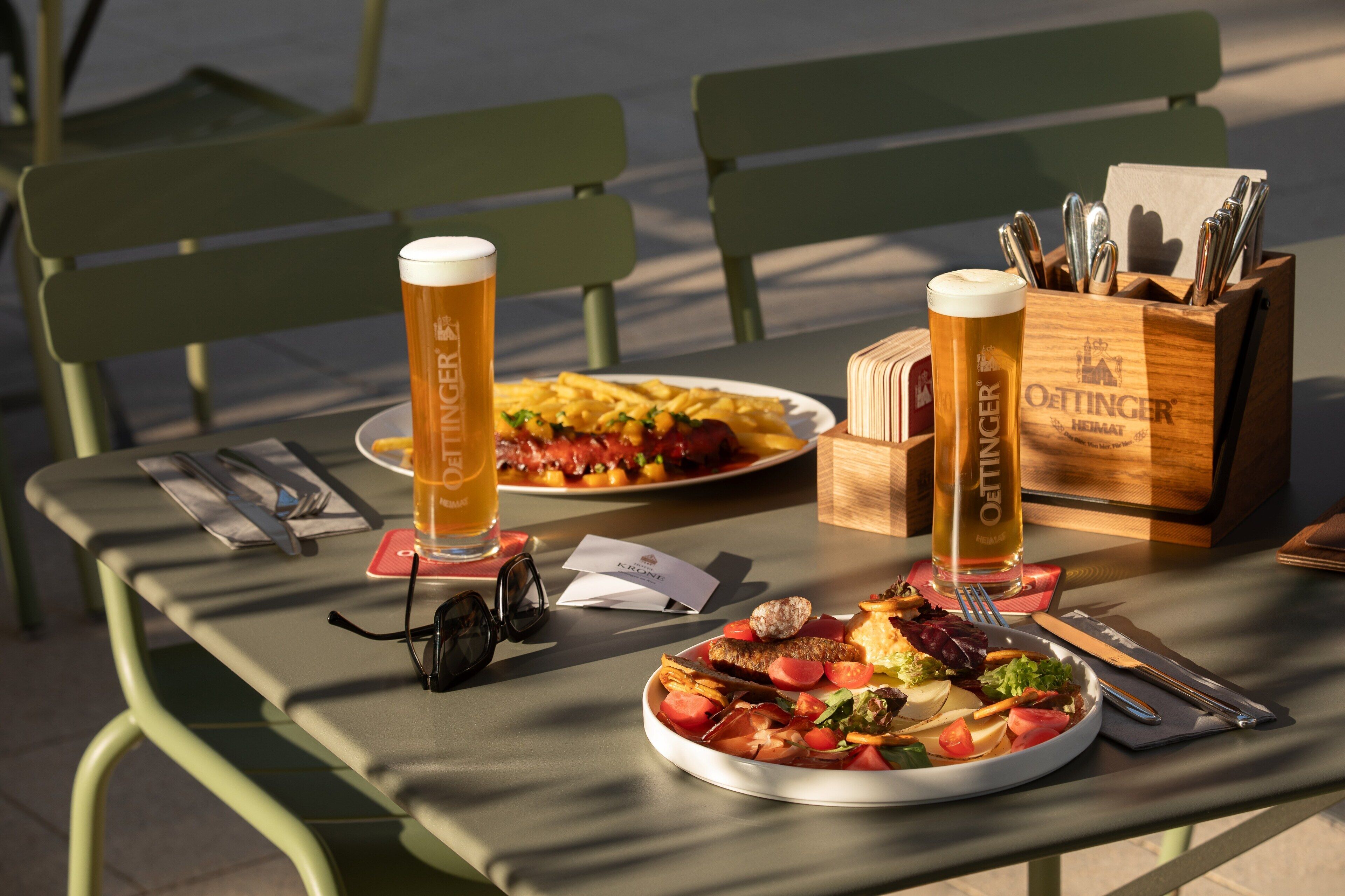 A table with two plates of food, two glasses of beer, and a knife block.