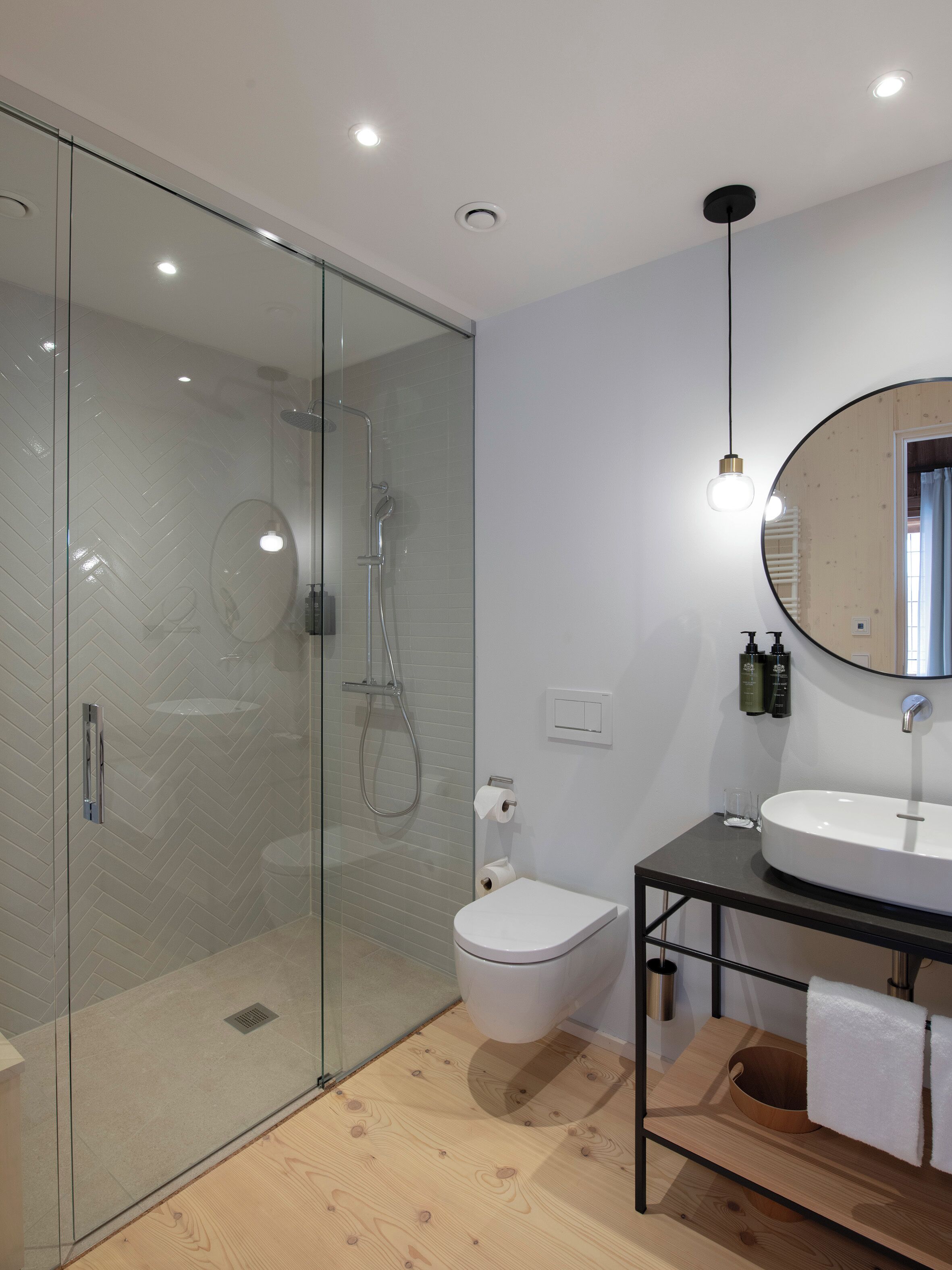 Ein modernes Badezimmer mit einer gläsernen Duschkabine, einer weißen Toilette, einem Holzwaschtisch mit Waschbecken und einem Spiegel.
