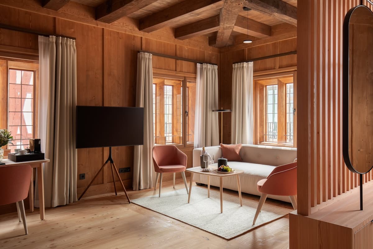 A cozy room with wooden walls, a flat-screen TV on a tripod stand, a white sofa, and two pink chairs.