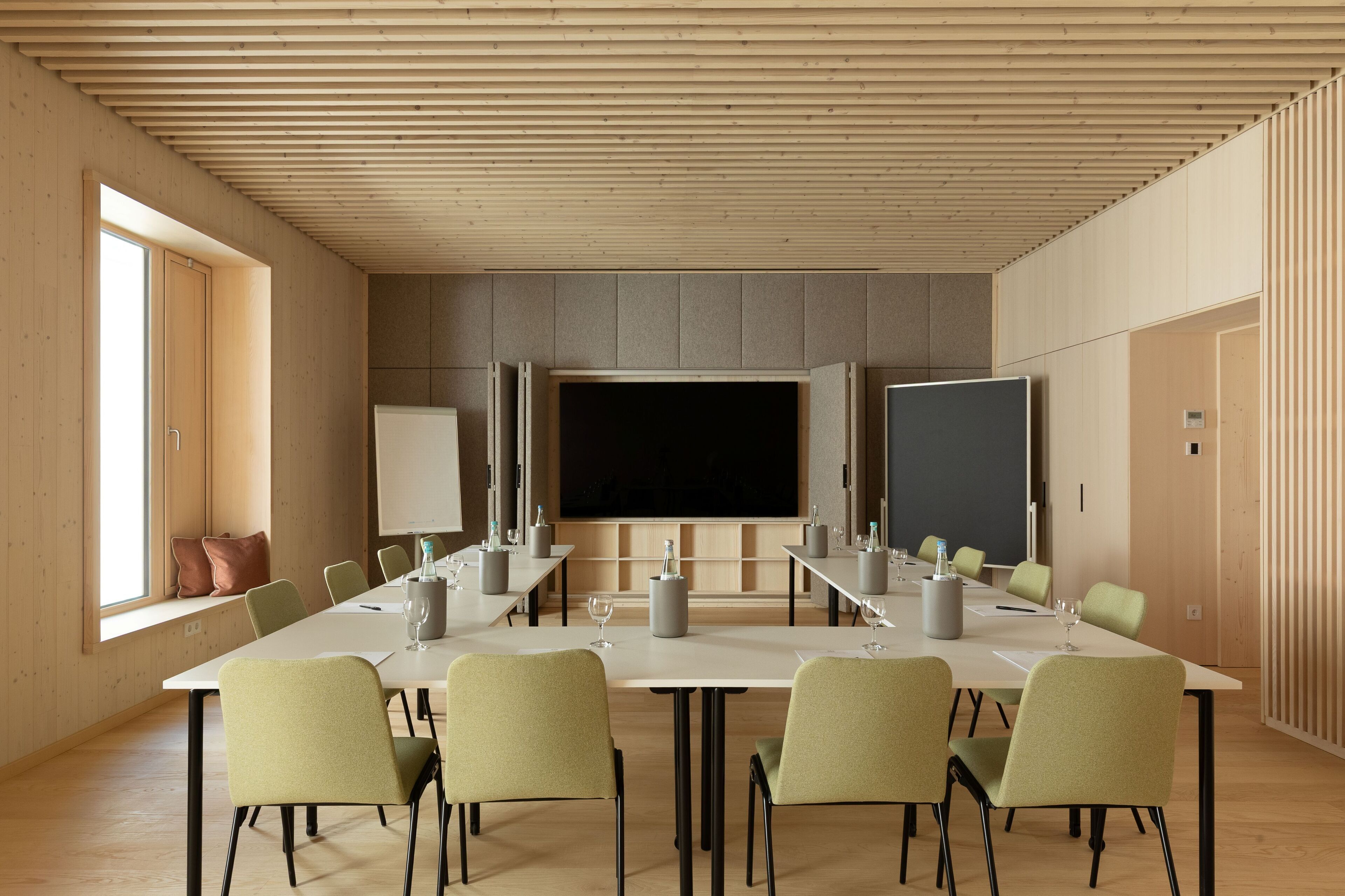 Uma sala de conferências com uma mesa comprida, várias cadeiras, uma tela grande e um quadro branco.