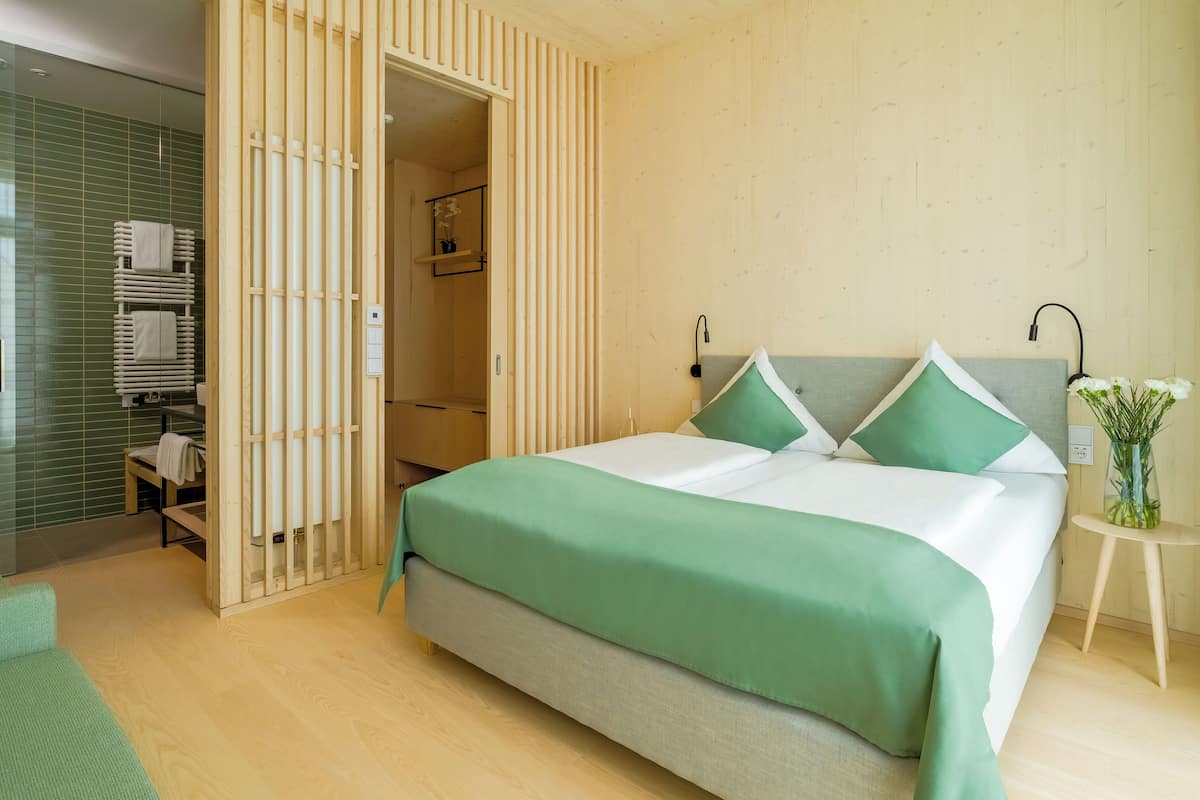 A modern bedroom with a large bed, a wooden wardrobe, and a small seating area.