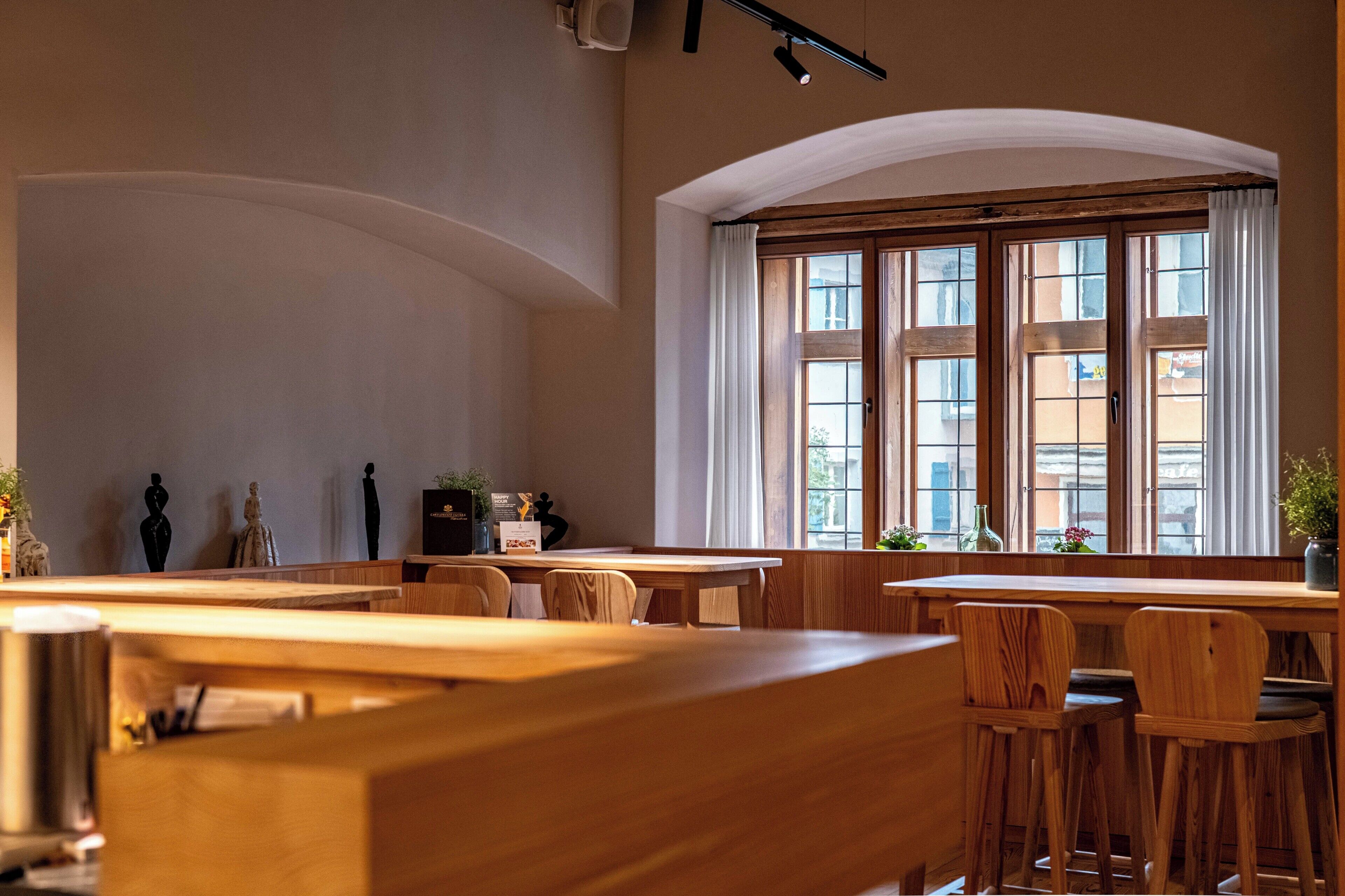 Un restaurant avec des tables et des chaises en bois, de grandes fenêtres avec des rideaux et un plafond haut.