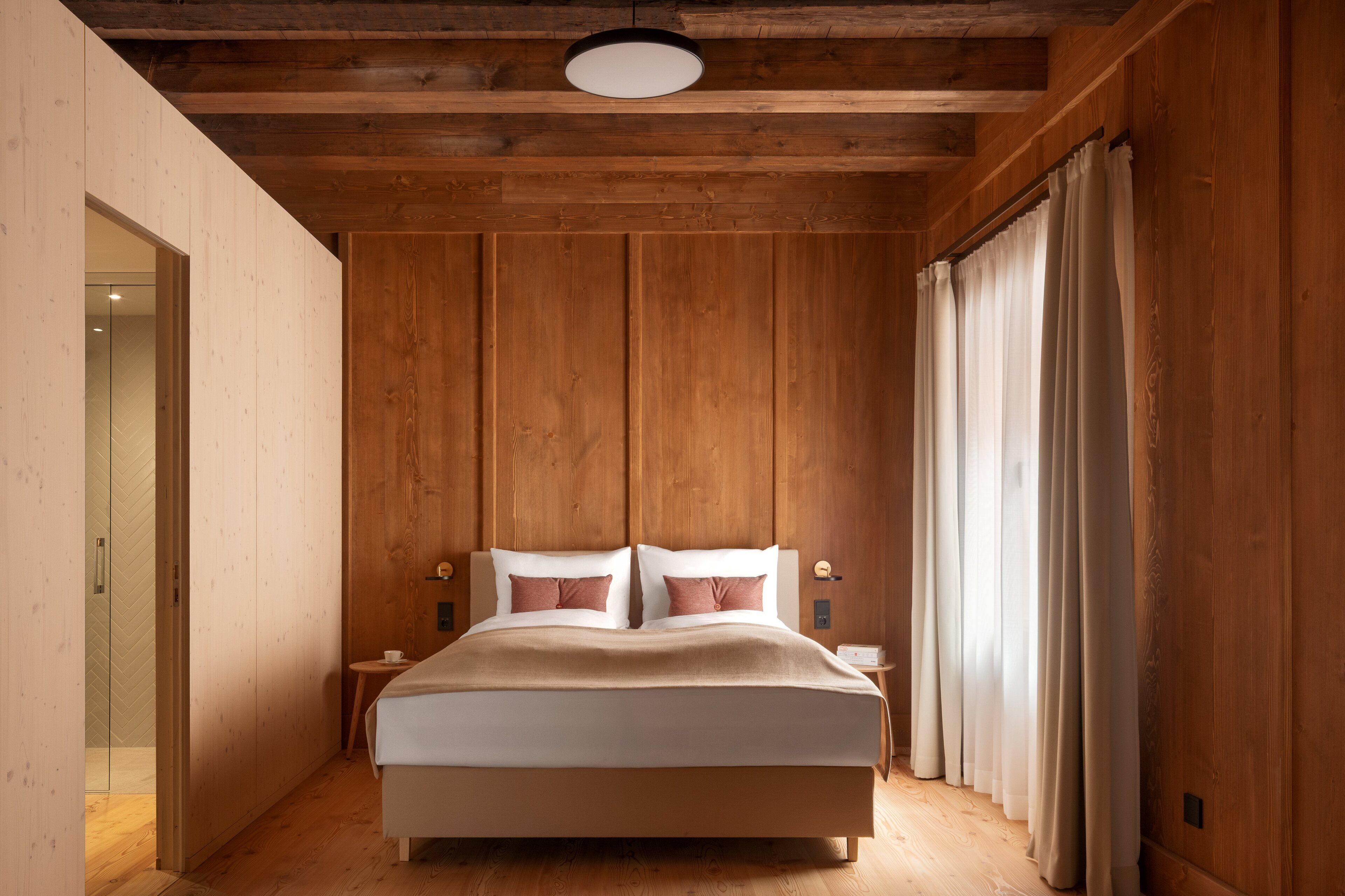 A bedroom with a wooden ceiling, a bed with white bedding, and a nightstand with a lamp.