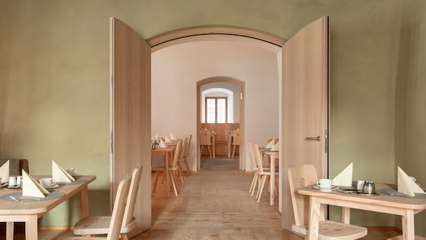 A room with a long table and chairs, a wooden floor, and a door leading to another room. - Hotel Krone (Oettingen in Bayern)