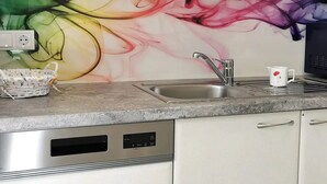 Een keuken met een kleurrijke abstracte muurschildering, een roestvrijstalen spoelbak, een magnetron en een mandje op het aanrecht.