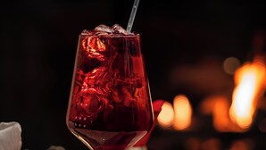 Eine Hand hält ein Weinglas mit Trinkhalm, Kerze und dekorativem Glas auf einem Tisch.