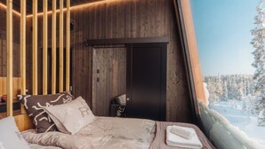 Ein Schlafzimmer mit einem Bett, Kissen, einem Nachttisch und einem Fenster mit Blick auf eine verschneite Landschaft.