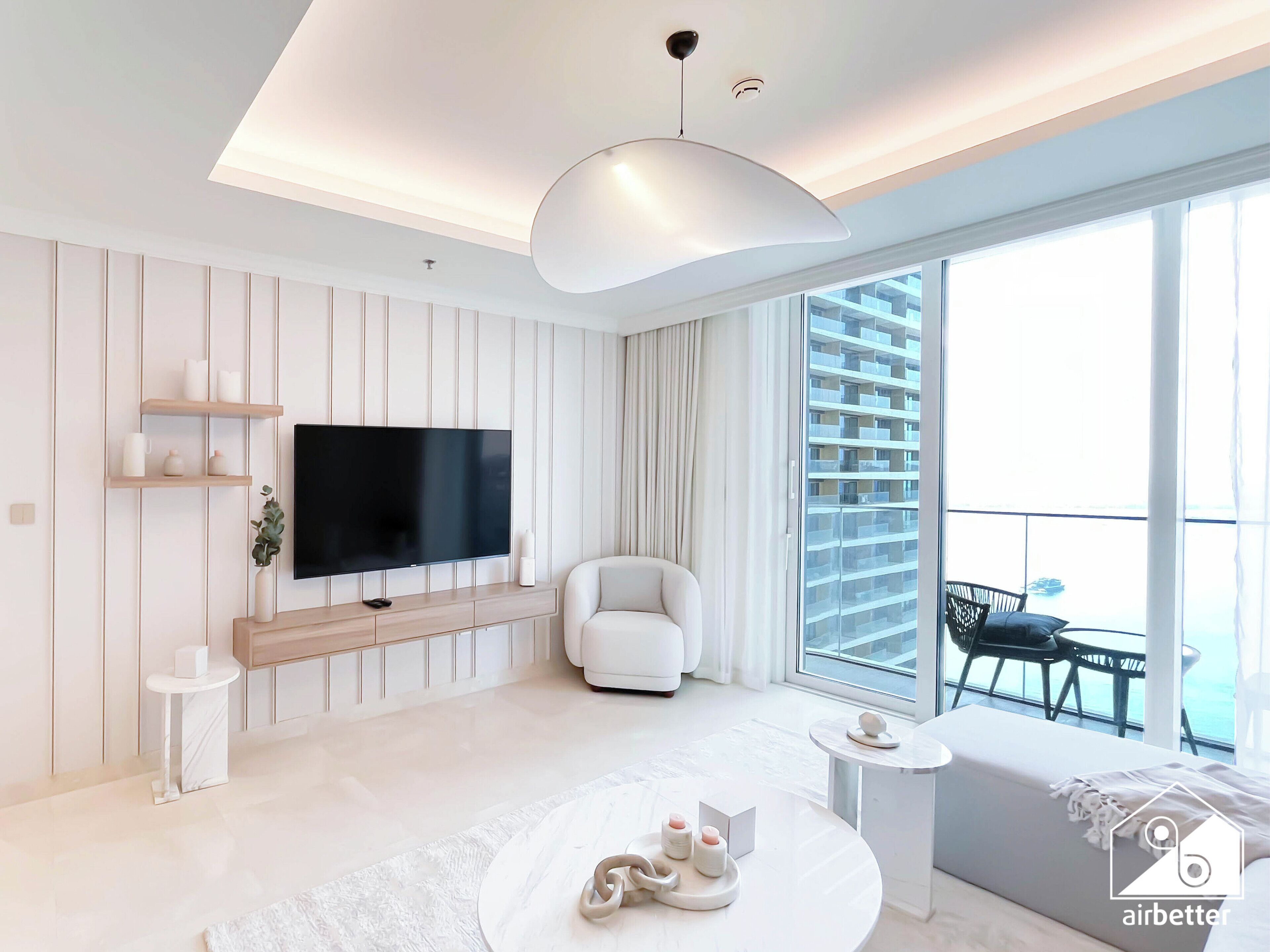 A modern living room with a flat-screen TV, white furniture, and a balcony with a view.