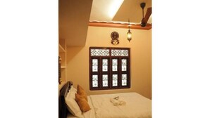 Une chambre à coucher avec un lit, des oreillers, une fenêtre ornée de barreaux en fer décoratifs et un luminaire fixé au mur.