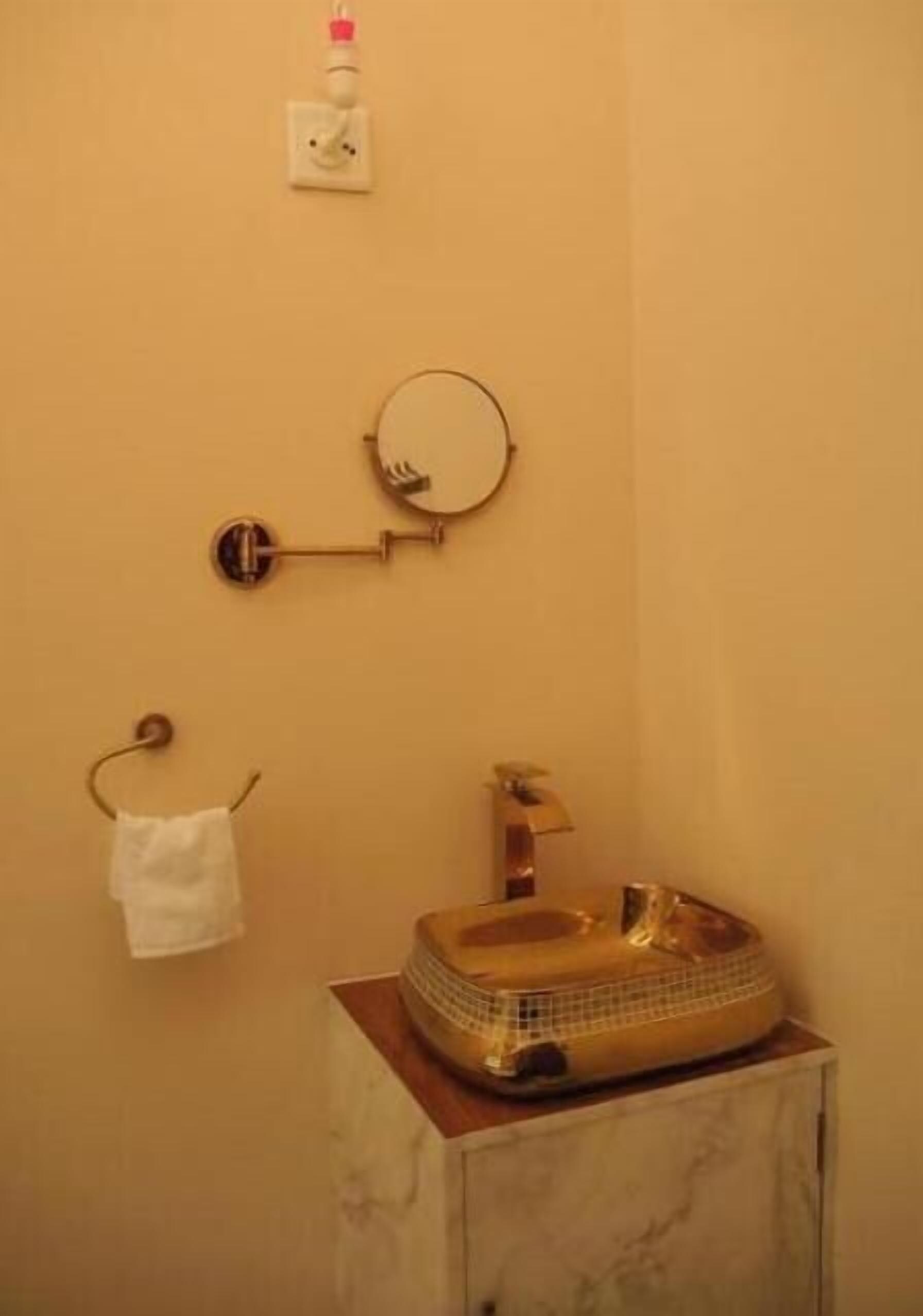 A bathroom with a gold sink, a towel rack, and a mirror.
