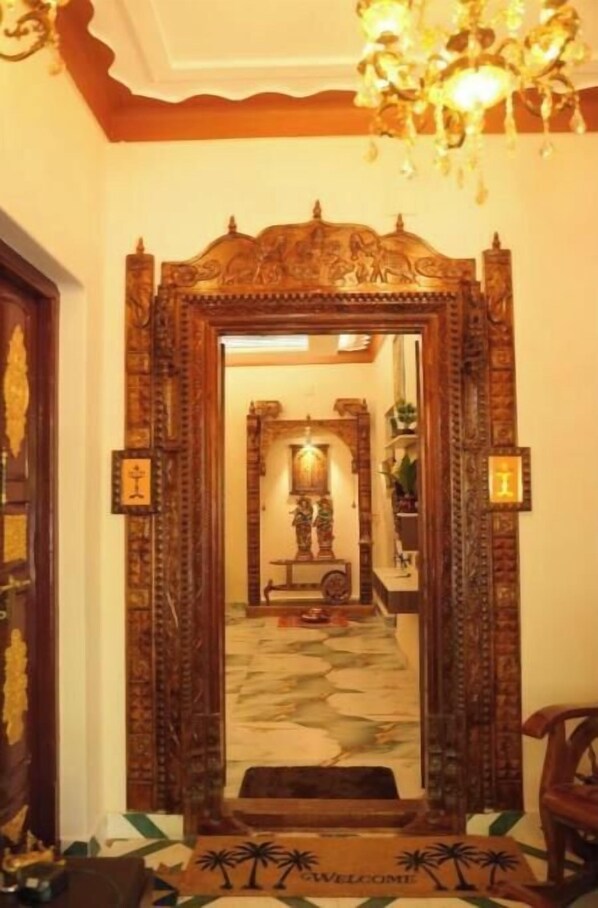 An ornate wooden entrance with a mirror, a chandelier, and a welcome mat.