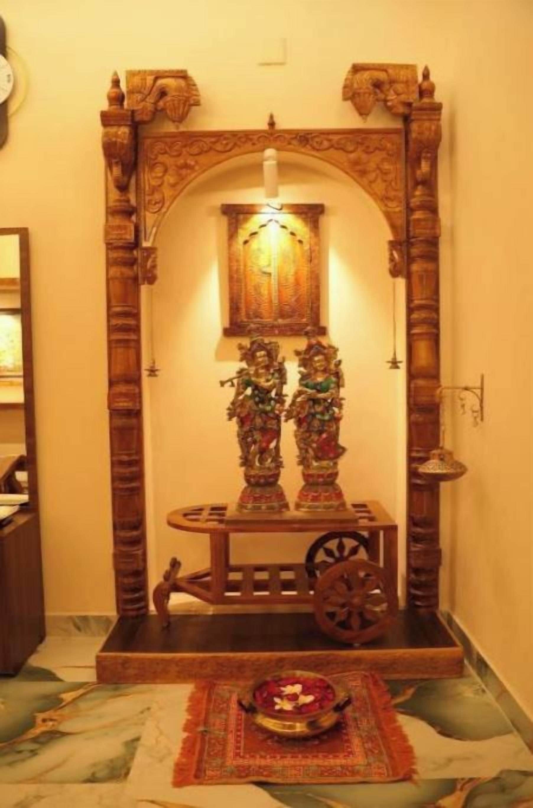 A traditional Indian shrine with a wooden arch, a small table with statues, and a lamp.