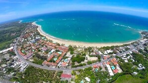 Vue aérienne d’une ville côtière avec une plage, des zones résidentielles et une route qui longe le littoral.