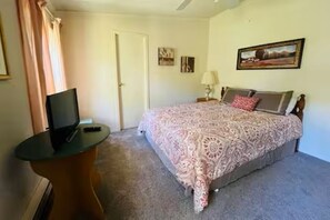 Une chambre à coucher avec un lit, un téléviseur posé sur une petite table et une porte.
