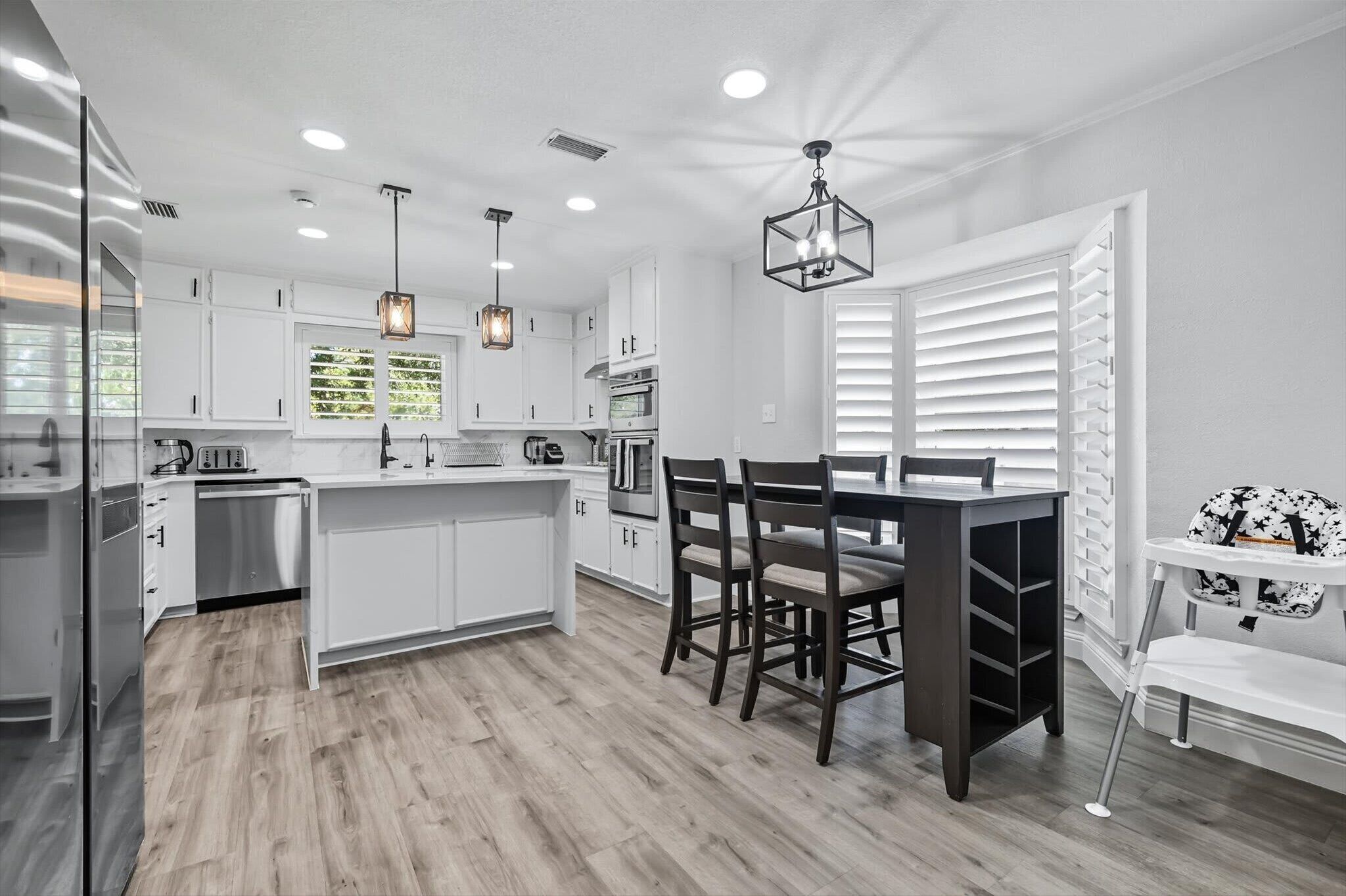 A modern kitchen with white cabinetry, a central island, pendant lighting, and a dining area with a table and chairs.
