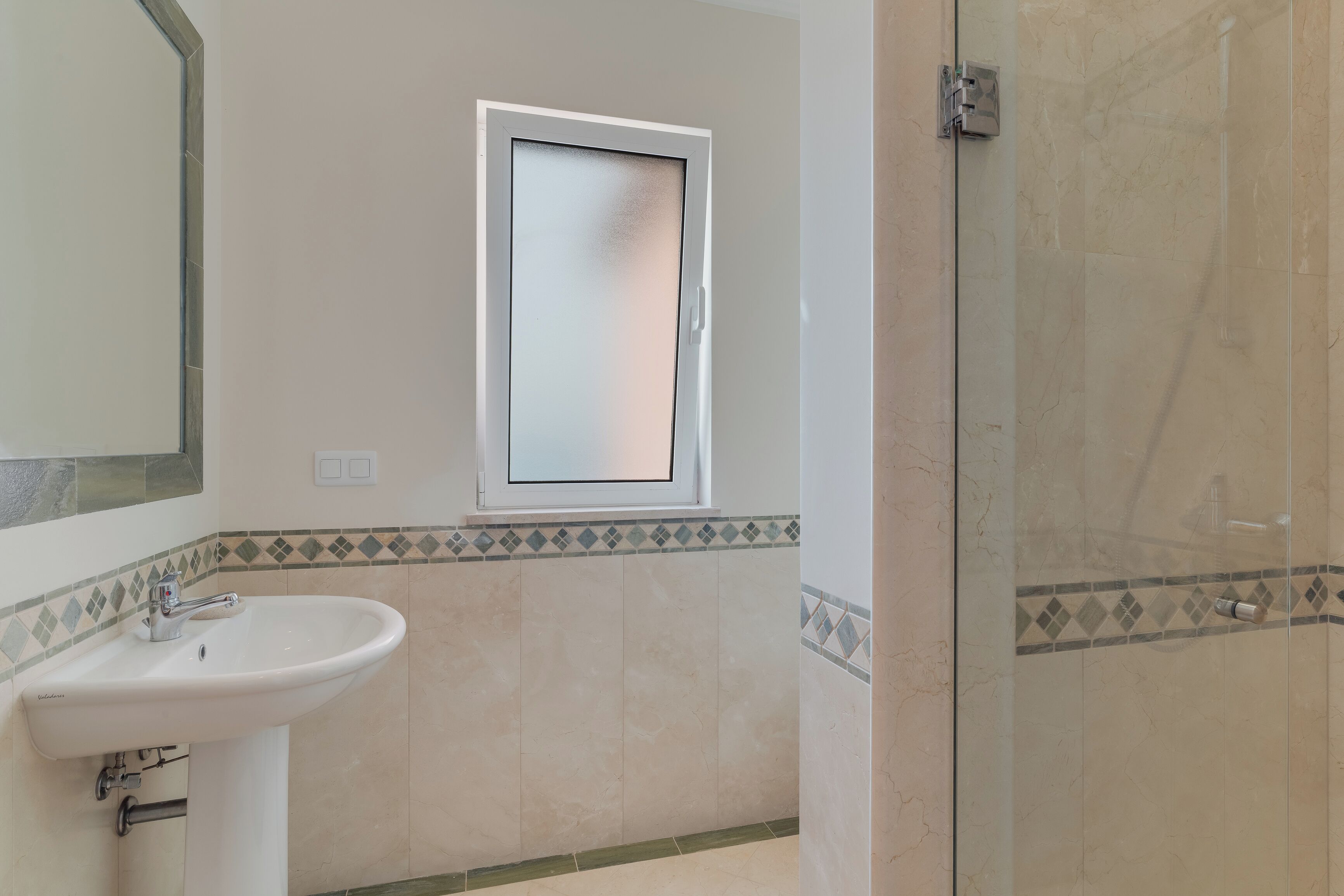 Une salle de bain équipée d’un lavabo, d’un miroir, d’une fenêtre et d’un espace douche.