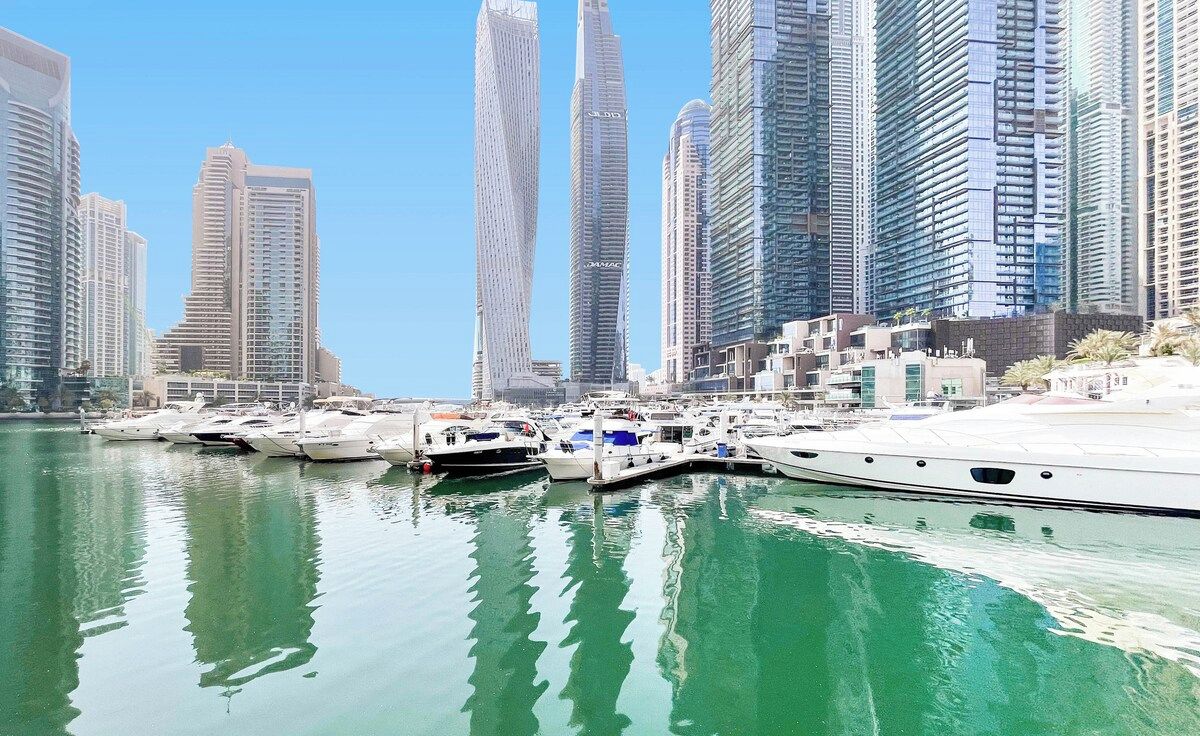 A marina with several yachts docked, surrounded by high-rise buildings.