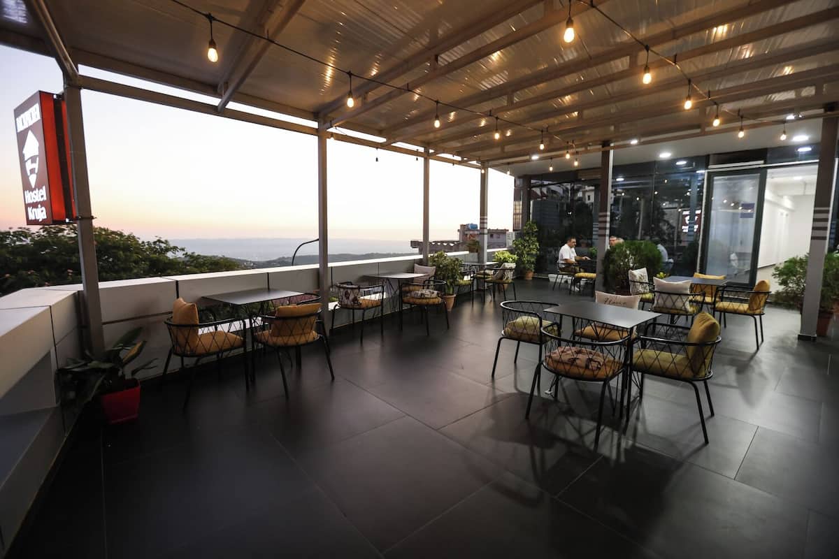 An outdoor patio area with tables and chairs, a sign indicating a hostel, and a view of the cityscape.
