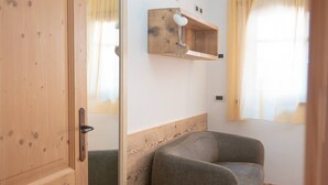 A room with a wooden door, a grey sofa, a wooden shelf with a heart-shaped lamp, and a window with curtains. - THE LADY OF THE LAKE (Molveno)