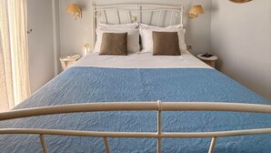 Un dormitorio con una cama, dos lámparas de noche, un espejo en la pared y una ventana con cortinas.