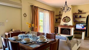 Un comedor con una mesa preparada para cuatro personas, chimenea, televisor y una zona de estar acogedora con sofá y sillón.