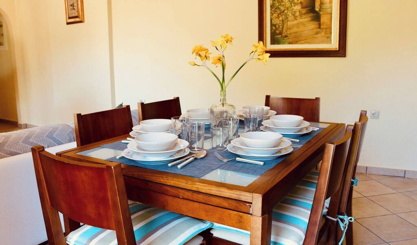A dining table set with plates, glasses, and cutlery, surrounded by wooden chairs with striped cushions.