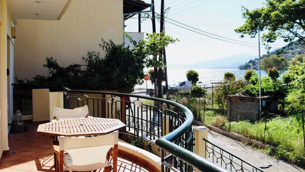 Un balcón con mesa y sillas, con vistas a un paisaje pintoresco de un lago y colinas.