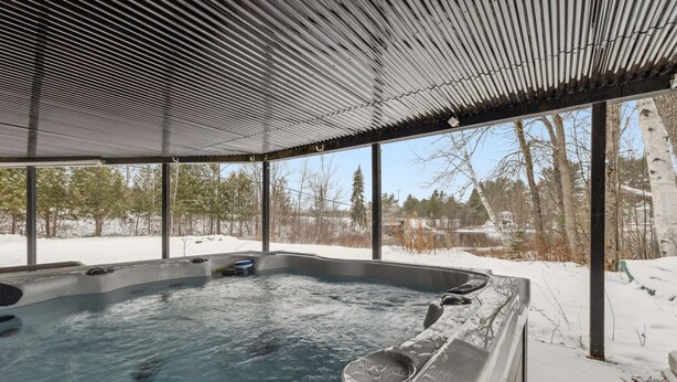 A hot tub with a metal roof and glass walls, surrounded by snow. - Water Front - Cozy Lakeside Getaway (Nominingue)