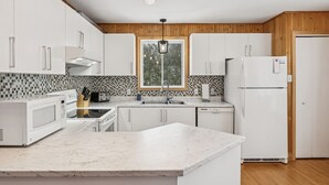 A modern kitchen with white cabinets, a large window, a built-in microwave, and a refrigerator. - Water Front - Cozy Lakeside Getaway (Nominingue)