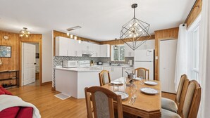 A modern kitchen with white cabinets, a central island, and a dining area with a wooden table and chairs. - Water Front - Cozy Lakeside Getaway (Nominingue)