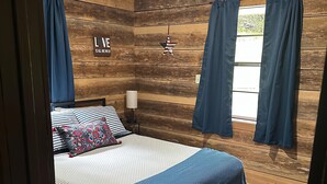 Quarto com parede de madeira, cama com colcha listrada, travesseiro com padrão floral e um letreiro com a palavra 'LOVE'.
