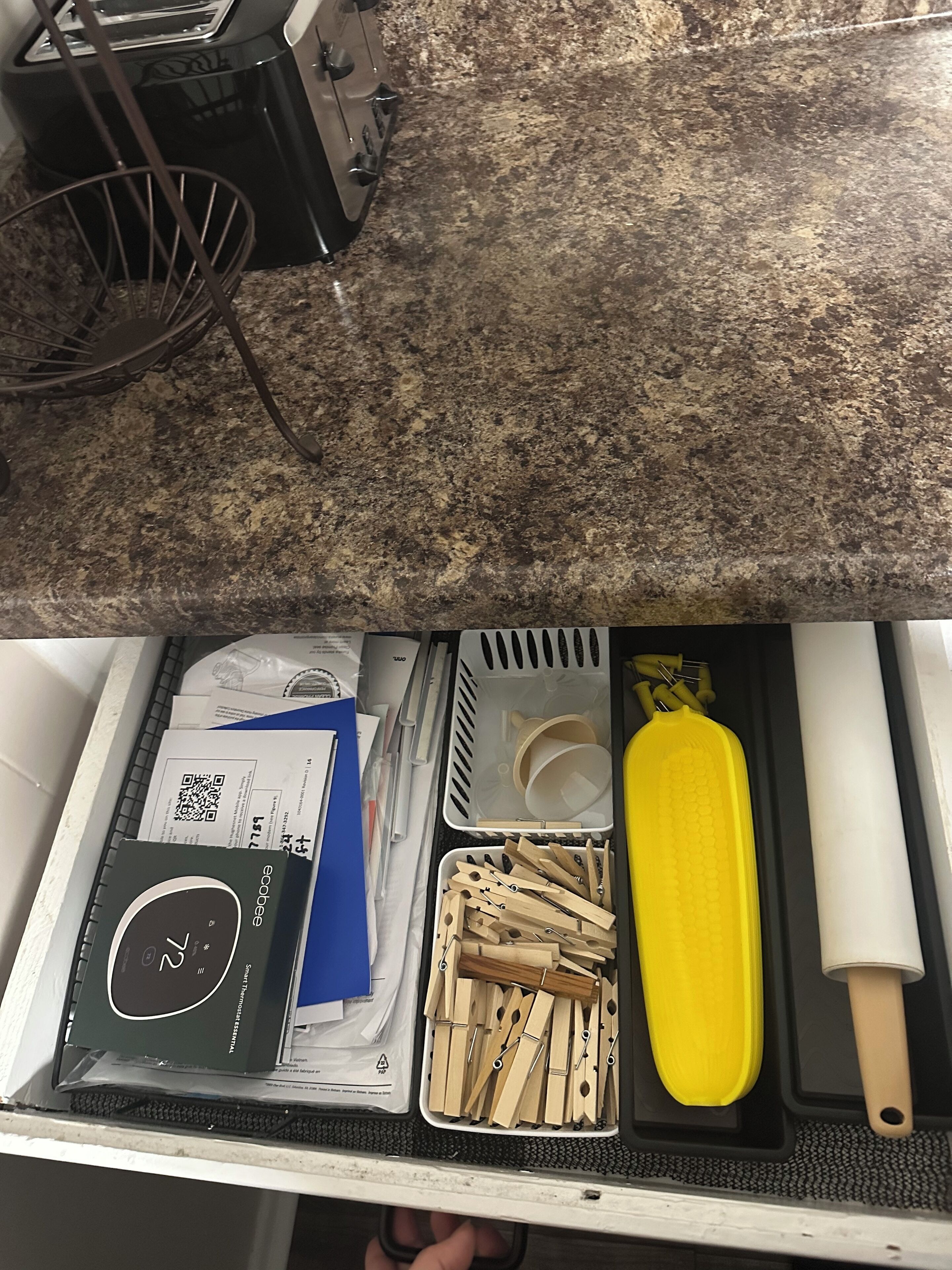 Una cocina con encimera de granito, un tostador y un cajón con productos de limpieza y utensilios.