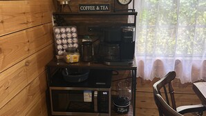 Interior acolhedor de uma cabana com parede de madeira, um canto para café, um relógio e vista para o verde lá fora.