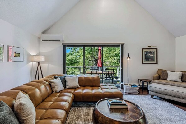 A living room with a brown leather sectional sofa, a grey sofa, a round coffee table, and a balcony with a red umbrella. - Luxury Snow Village Ski-In/Out, Golf & Club Access (Hartford)