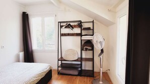 Ein Schlafzimmer mit Etagenbett, Standventilator, Heizkörper und einem Fenster mit Vorhängen.