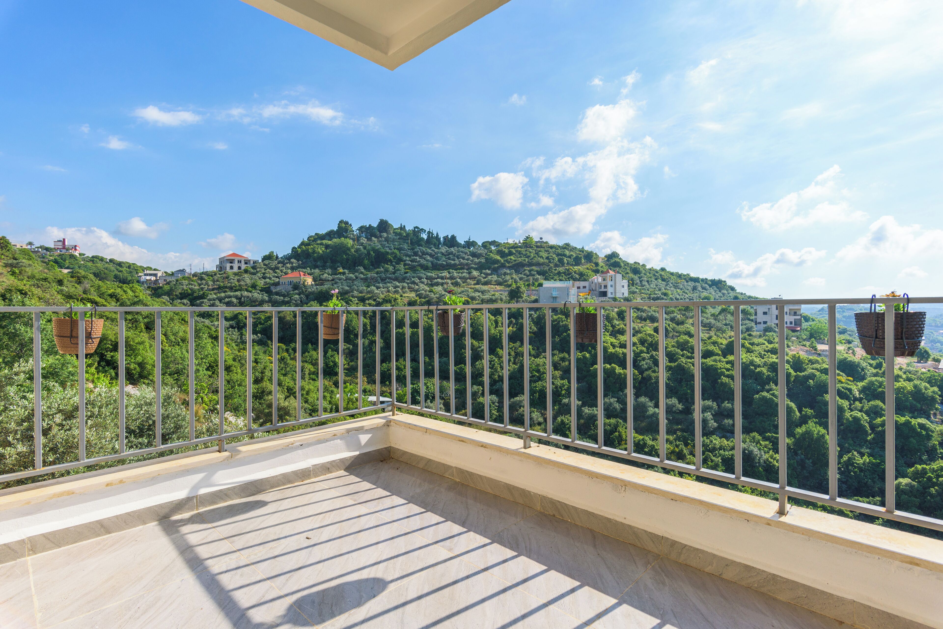 A balcony with a metal railing overlooking a hillside with buildings and greenery.