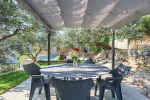 Eine Terrasse im Freien mit einem runden Tisch und Stühlen, umgeben von Grünpflanzen und einer Steinmauer.