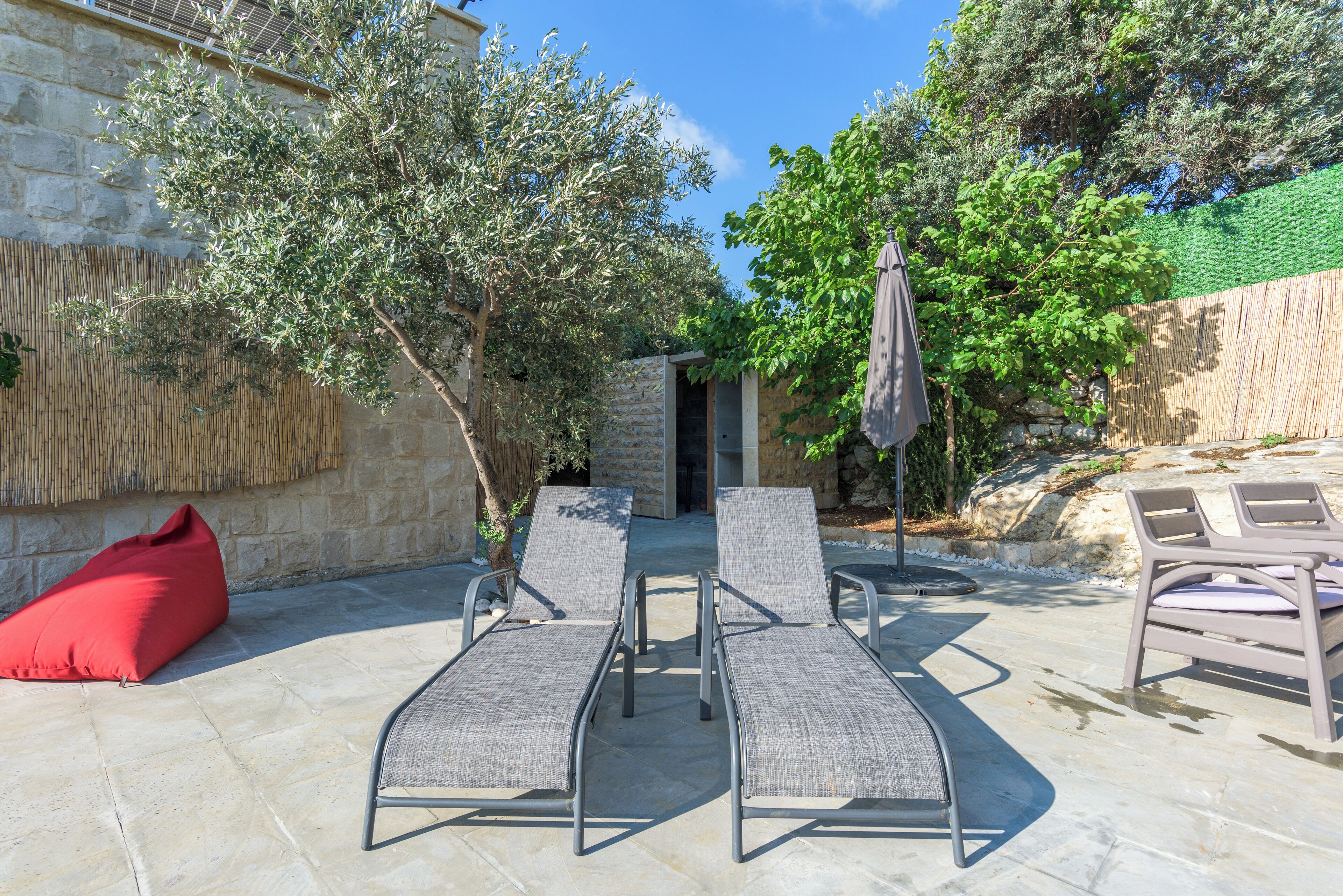 A patio with lounge chairs, a red bean bag, and a stone wall.