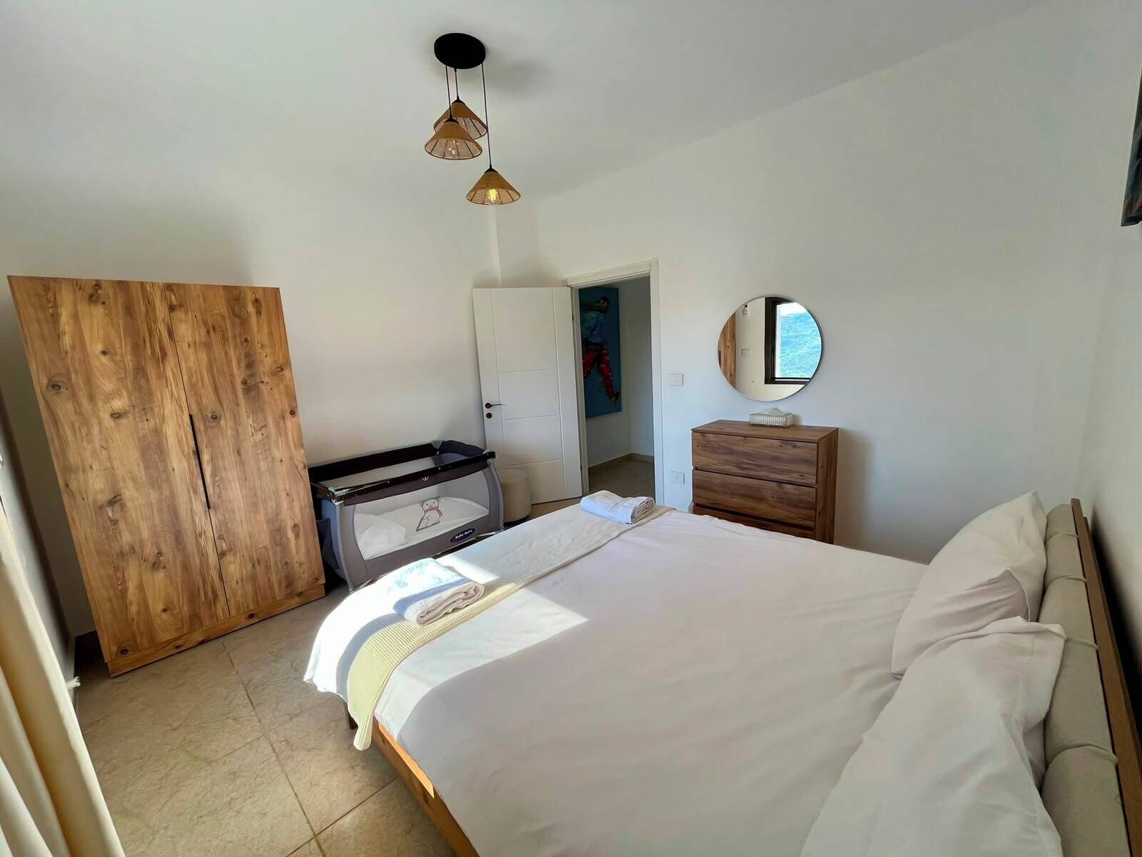 A bedroom with a bed, a wooden wardrobe, a dresser, a mirror, and a crib.